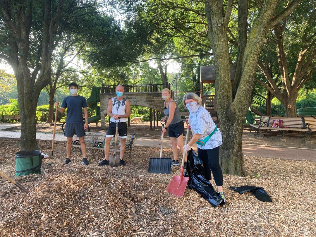 Friends of Rose Park volunteers wear masks stand with shovels and rakes on wood chips they are working to spread.