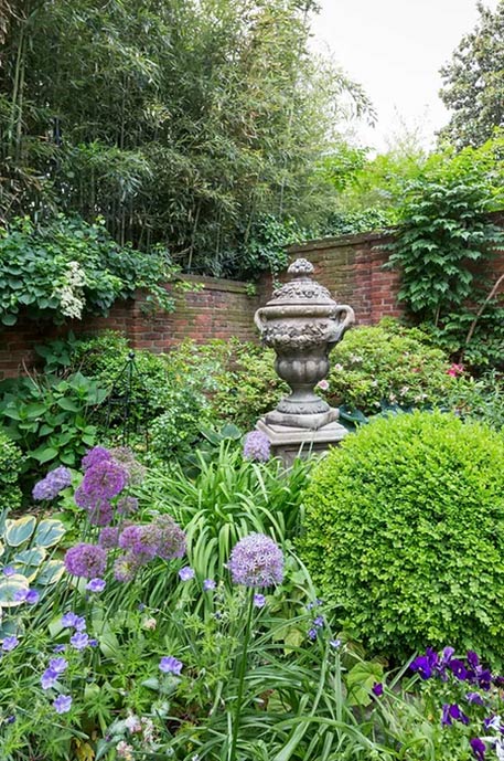 Georgetown Garden Club - Friends of Rose Park Community Partner - image of a garden with purple flowers and scultpure with a brick wall shrouded in ivy behind it